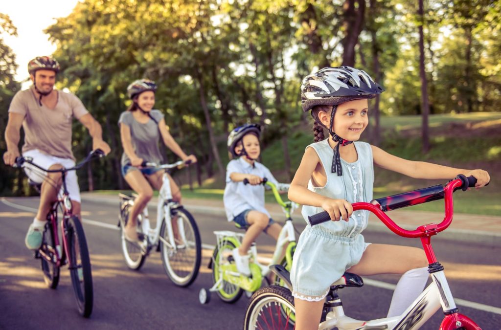 Szczęśliwa rodzina jeździ na rowerach na świeżym powietrzu i uśmiecha się. Mała dziewczynka na pierwszym planie